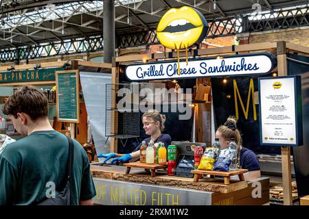 Gli chef preparano panini al formaggio grigliato in una bancarella all'interno dell'Old Spitalfileds Market, Londra E1 Foto Stock