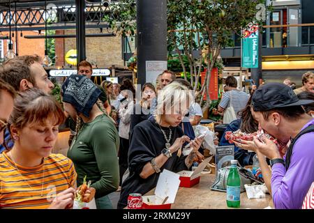 Persone che si godono il cibo di vari venditori di cibo presso la food hall nell'Old Spitalfields Market, Londra E1 Foto Stock