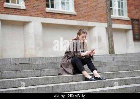 Donna che mantiene smart phone su scala Foto Stock