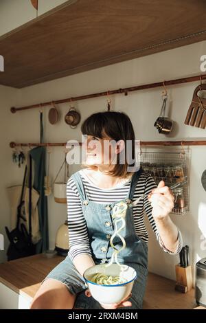 Donna con ciotola di noodle di zucchine sulla panca da cucina Foto Stock