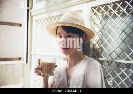 Giovane donna che indossa un cappello di paglia che regge un caffè ghiacciato Foto Stock