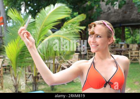 Giovane donna che indossa un bikini con fiori sulla sua testa tenendo selfie Foto Stock