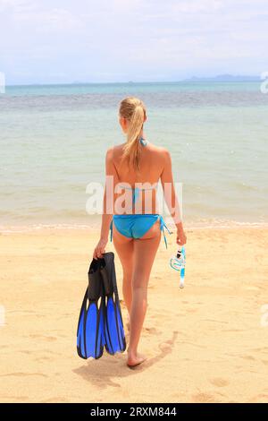 Giovane donna che indossa un bikini azienda pinne sulla spiaggia Foto Stock