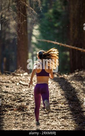 Vista posteriore della giovane donna in esecuzione nella foresta Foto Stock