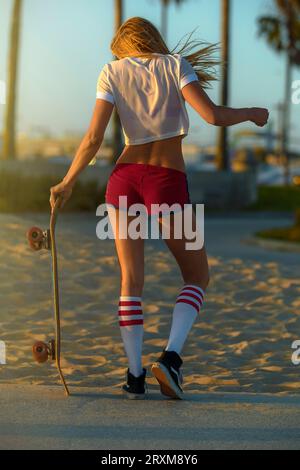 Vista posteriore della giovane donna con lo skateboard in spiaggia Foto Stock