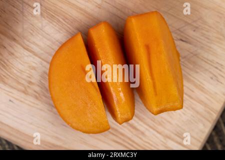 Il persimmon snocciolato d'arancia maturo a fette è sdraiato sul tavolo, i frutti del persimmon d'arancia sono tagliati a fettine Foto Stock