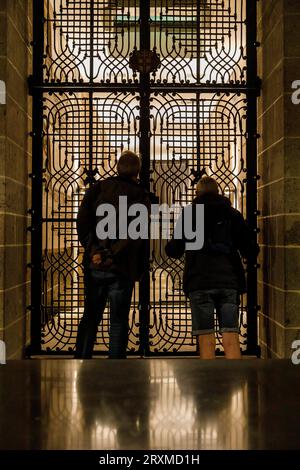 I visitatori guardano attraverso un reticolo nella cripta della cattedrale presso la tomba degli Arcivescovi di Colonia, Colonia, Germania. Besucher Schauen in der Kry Foto Stock