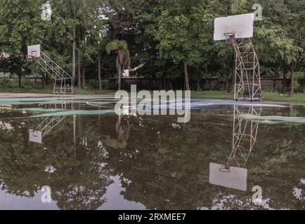 Due tabelloni da basket in legno con anelli in metallo e la rete bianca mostrano il loro riflesso sull'acqua piovana in tutto il vecchio basket Foto Stock