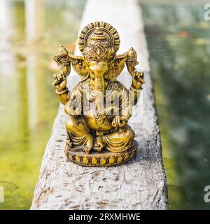 Statua di Ganesha d'oro su un tronco sopra l'acqua. Foto Stock