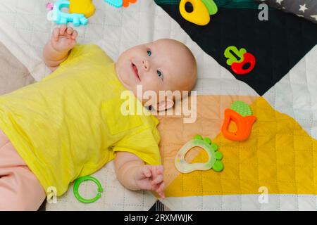 Piccolo e carino, circondato da giocattoli colorati, sdraiato a casa sul letto Foto Stock