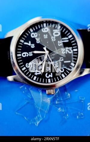 Orologio con vetro dello schermo incrinato su sfondo blu Foto Stock