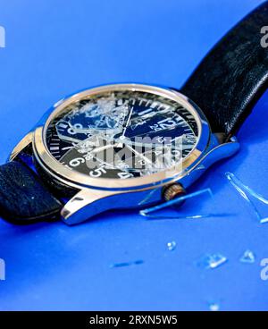 Orologio con vetro dello schermo incrinato su sfondo blu Foto Stock