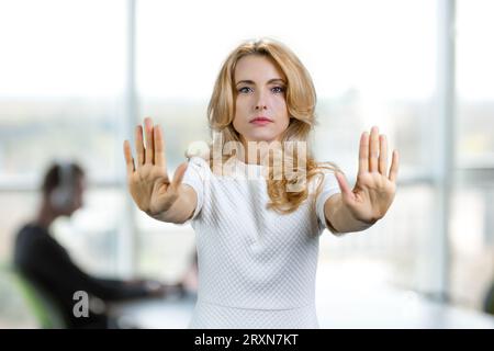 Ritratto di una donna bionda matura seria che fa uno stop con entrambe le mani. Interni di uffici sullo sfondo. Foto Stock