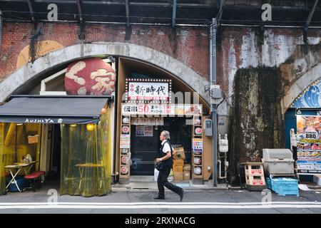 Un giapponese cammina davanti a un ristorante colorato a Shimbashi, Tokyo, Giappone Foto Stock