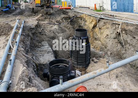 Vista della ricostruzione stradale con un'ampia trincea, tubi del sistema di drenaggio e nuovi pozzetti di ispezione in plastica Foto Stock