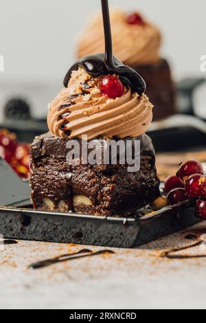 Brownie su piatti neri e decorati con cioccolatini, sciroppo di cioccolato e frutti di bosco. Su uno sfondo grigio di cemento. Foto Stock