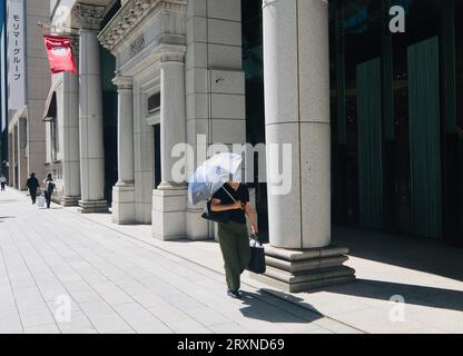 Una donna illuminata dal sole che tiene un ombrello cammina lungo il marciapiede di Nihonbashi, Tokyo, Giappone Foto Stock