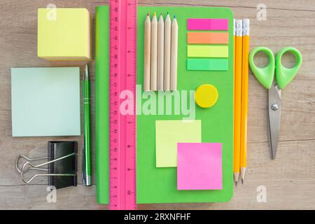 Appunti post-it, un righello, una penna, matite, forbici e un pianificatore verde luminoso ordinato su un tavolo di legno. cancelleria sul tavolo Foto Stock