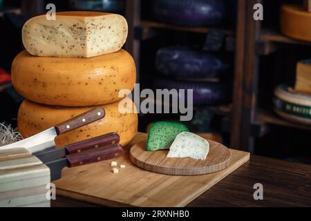 Le teste di formaggio con fette e coltelli giacciono su una tavola di legno con un interno. Foto Stock