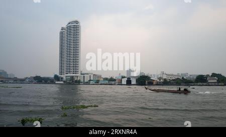 Bangkok, Thailandia, 28 dicembre 2018. Sotto un cielo coperto, un'alta struttura bianca si erge accanto a un fiume turbolento, dove una barca con un vulcano cremisi sa Foto Stock