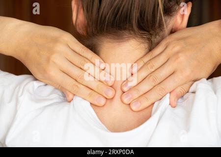 Una ragazza tiene le mani dietro il collo a casa, mal di collo, dolore acuto al collo Foto Stock