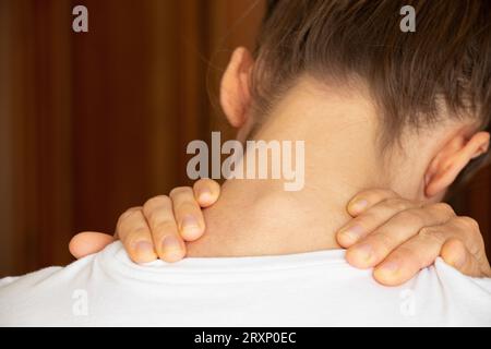 Una ragazza tiene le mani dietro il collo a casa, mal di collo, dolore acuto al collo Foto Stock