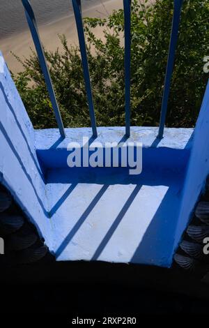 Balcone in legno dipinto di blu con ringhiere che gettano ombre in un'architettura di stile mediterraneo Foto Stock