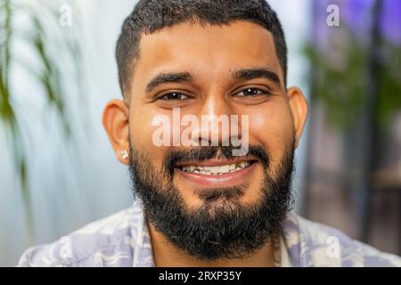 Ritratto di un uomo indiano felice e calmo a casa sul divano sorridente, piacevole espressione che guarda lontano sognando riposando, rilassandosi sentirsi soddisfatti buone notizie, festeggiare la vittoria. Giovane arabo in salotto Foto Stock