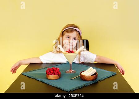 Una bambina carina che sembra infelice, non le è permesso mangiare il dessert sul tavolo davanti a lei. Il concetto di celebrazione. Foto Stock