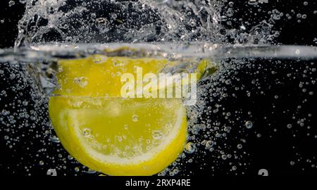 Sott'acqua di limonata dolcificata appena spremuta che affetta di limoni crudi cadendo in acqua soda su sfondo blu scuro o nero. Primo piano, Lemonad Foto Stock