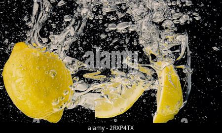 Sott'acqua di limonata dolcificata appena spremuta che affetta di limoni crudi cadendo in acqua soda su sfondo blu scuro o nero. Primo piano, Lemonad Foto Stock