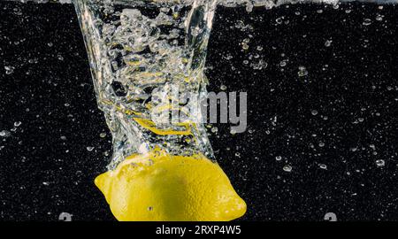 Sott'acqua di limonata dolcificata appena spremuta che affetta di limoni crudi cadendo in acqua soda su sfondo blu scuro o nero. Primo piano, Lemonad Foto Stock