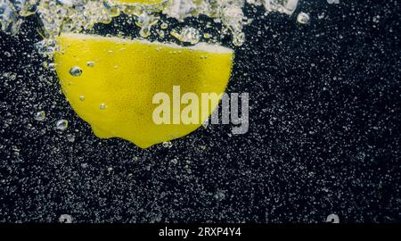 Sott'acqua di limonata dolcificata appena spremuta che affetta di limoni crudi cadendo in acqua soda su sfondo blu scuro o nero. Primo piano, Lemonad Foto Stock