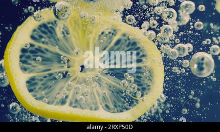 Sott'acqua di limonata dolcificata appena spremuta che affetta di limoni crudi cadendo in acqua soda su sfondo blu scuro o nero. Primo piano, Lemonad Foto Stock