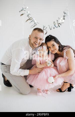 Genitori gioiosi che abbracciano la figlia nell'arredamento di compleanno Foto Stock