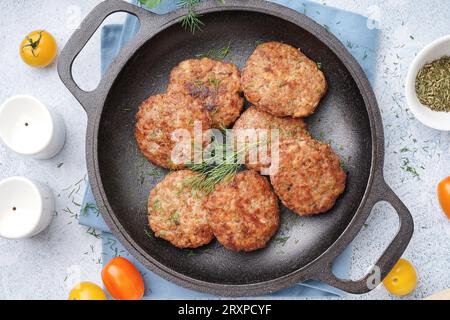 Padella con cotolette, aneto e pomodori sul tavolo blu grunge in cucina Foto Stock