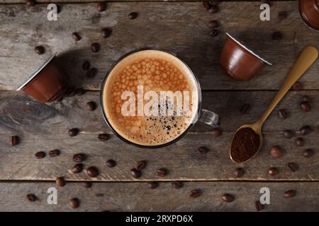 Tazza di delizioso caffè, capsule e fagioli su un tavolo di legno Foto Stock