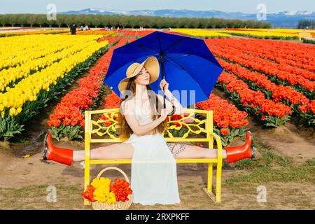 Bruna a pelo lungo che si divide sulla panca di fronte al campo di tulipano Foto Stock