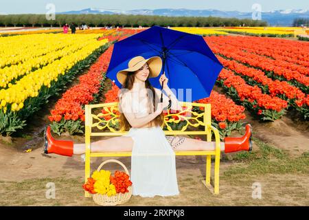 Bruna a pelo lungo che si divide sulla panca di fronte al campo di tulipano Foto Stock