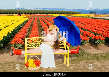 Bruna a pelo lungo che si divide sulla panca di fronte al campo di tulipano Foto Stock