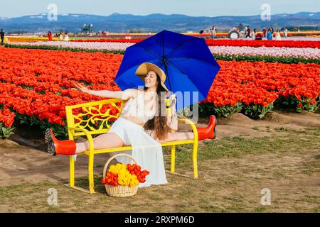 Bruna a pelo lungo che si divide sulla panca di fronte al campo di tulipano Foto Stock