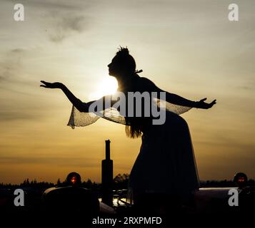 Silhouette di donna in piedi contro il tramonto con cesto in mano Foto Stock