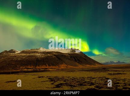 Aurora boreale e massicce montagne in Islanda. L'aurora boreale luminosa crea un incredibile paesaggio nordico sotto le stelle del cielo. Colorato fenomeno magico con colline, fotografia notturna. Foto Stock