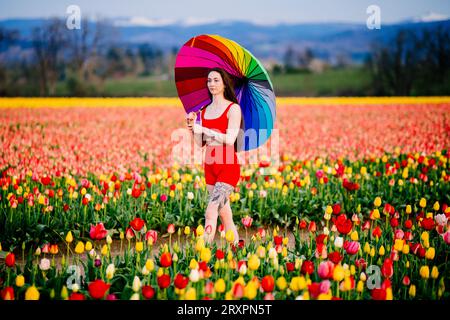 Bruna a pelo lungo che cammina attraverso un vasto campo di tulipani con ombrello in mano Foto Stock