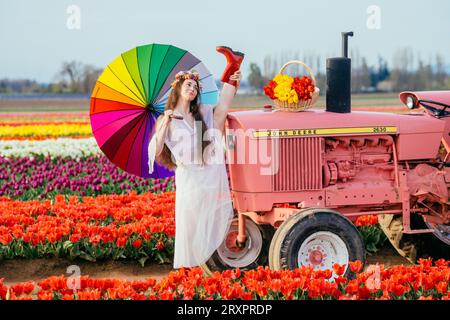 Donna che tiene un ombrello colorato mentre si divide sopra un trattore arrugginito Foto Stock