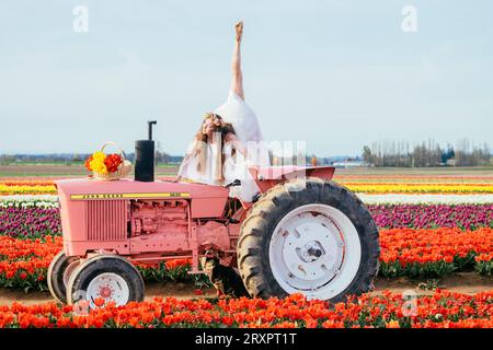 Donna che tiene un ombrello colorato mentre si divide sopra un trattore arrugginito Foto Stock