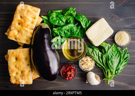 Ingredienti del sandwich Veggie tostato italiano su un tavolo di legno: Melanzane fresche, basilico, focaccia e altri ingredienti mediterranei Foto Stock