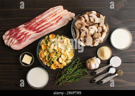 Orecchiette con salsa Thyme di funghi ingredienti: Orecchiette, pancetta, funghi e altri ingredienti su un tavolo di legno Foto Stock