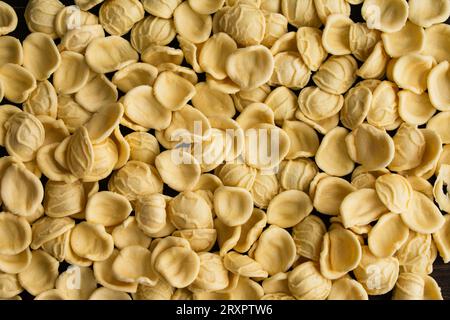 Pasta di orecchiette gialle secche sparse su un tavolo di legno: Pezzi di orecchiette crude su fondo di legno scuro Foto Stock