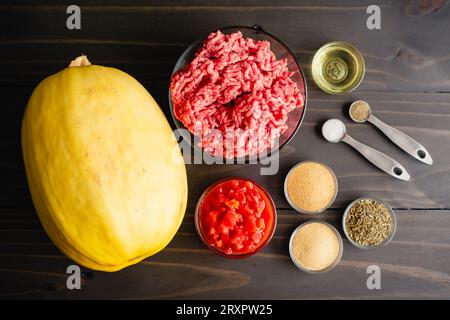 Spaghetti squash Bolognese ingredienti su un tavolo di legno: Manzo macinato, zucca intera, pomodori a dadini e altri ingredienti Foto Stock